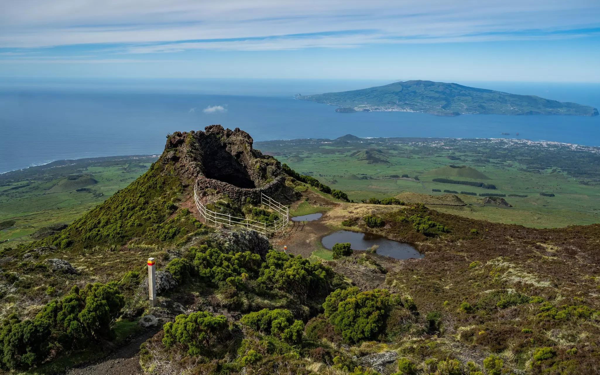 Aerial view of steep staircase leading to a rocky cave with the ocean and and island in the distance on a mostly sunny day.