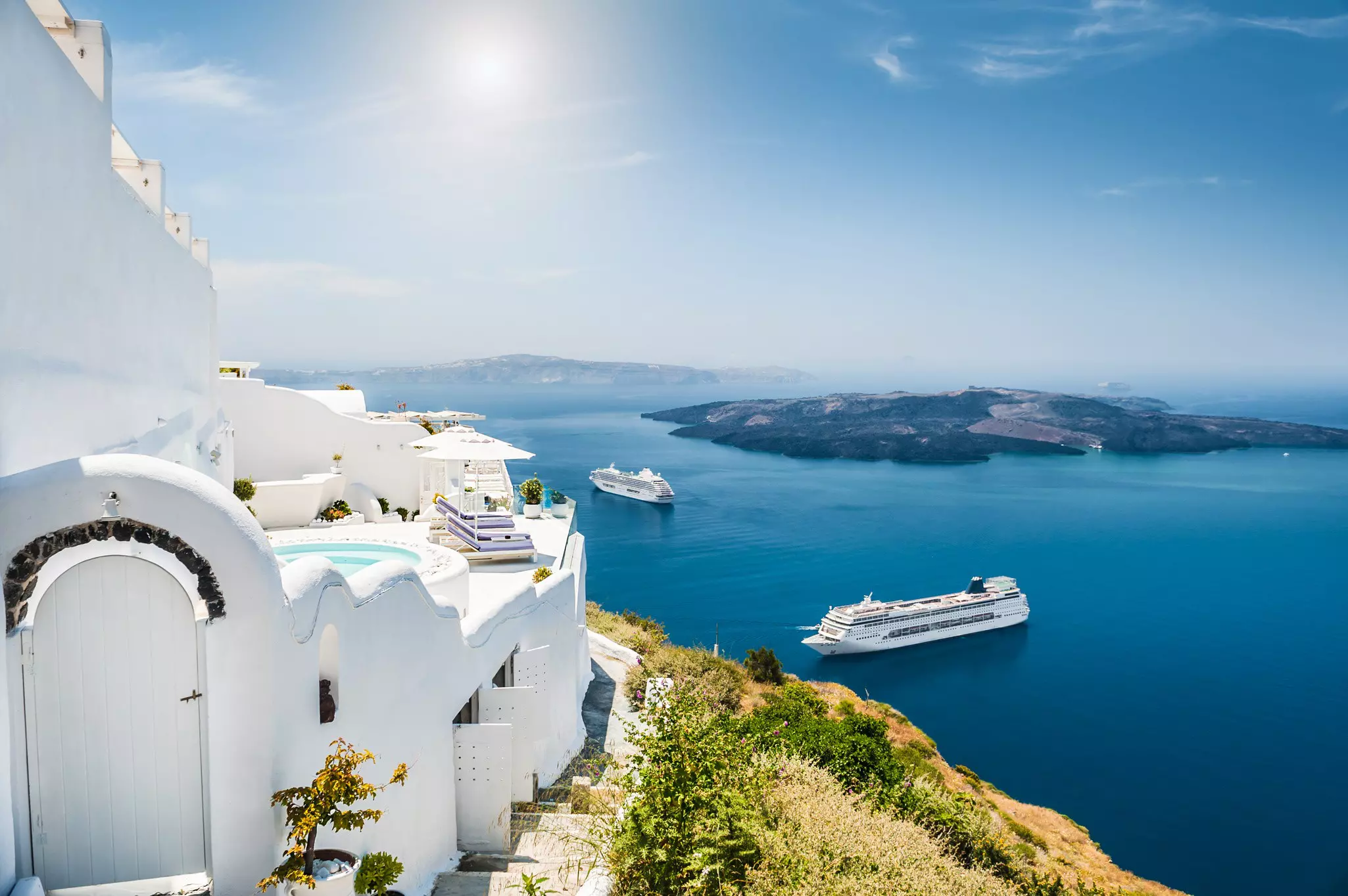 Two cruise ships in vividly blue waters off a coast with white buildings