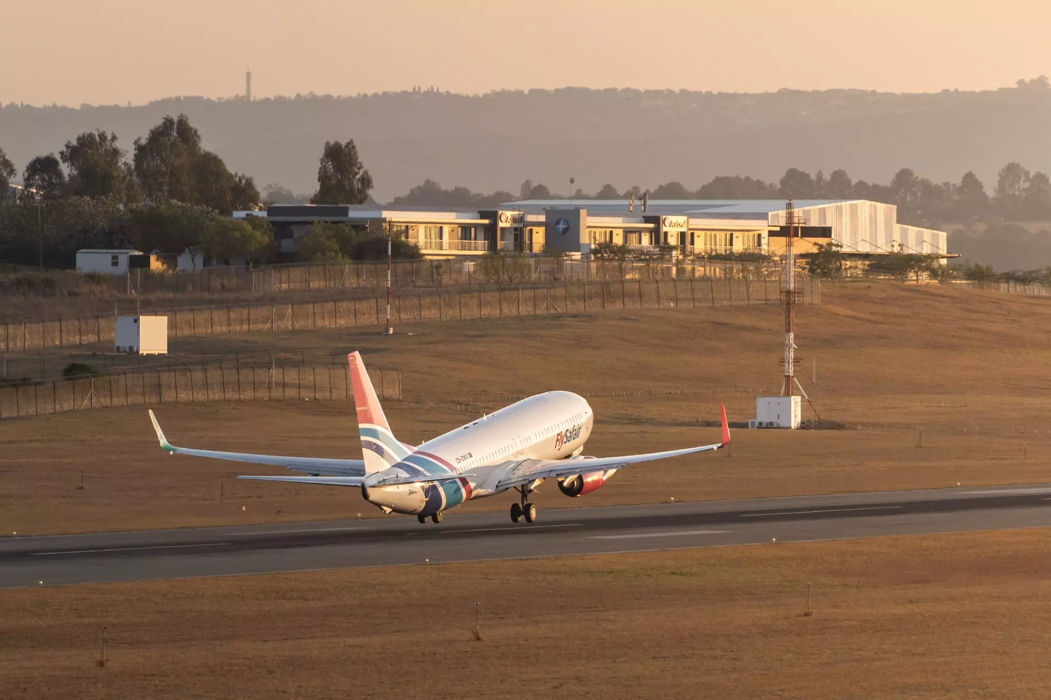 A small plane takes off on a runway bathed in low sunlight.