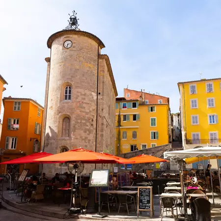 An ancient tower with a clock surrounded by yellow buildings in a historic old town. 