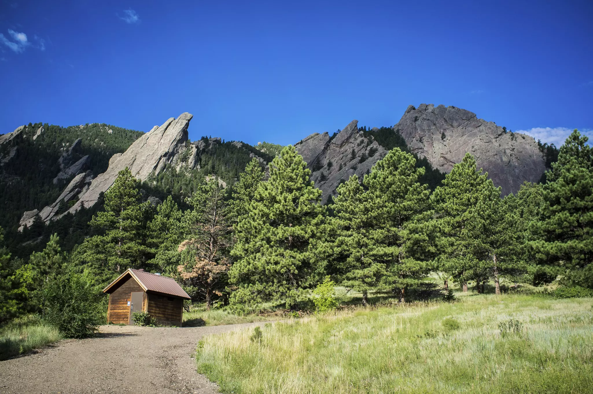 The Flatiron mountain formation forms the backdrop, with a small hut and paved trail in the foreground.