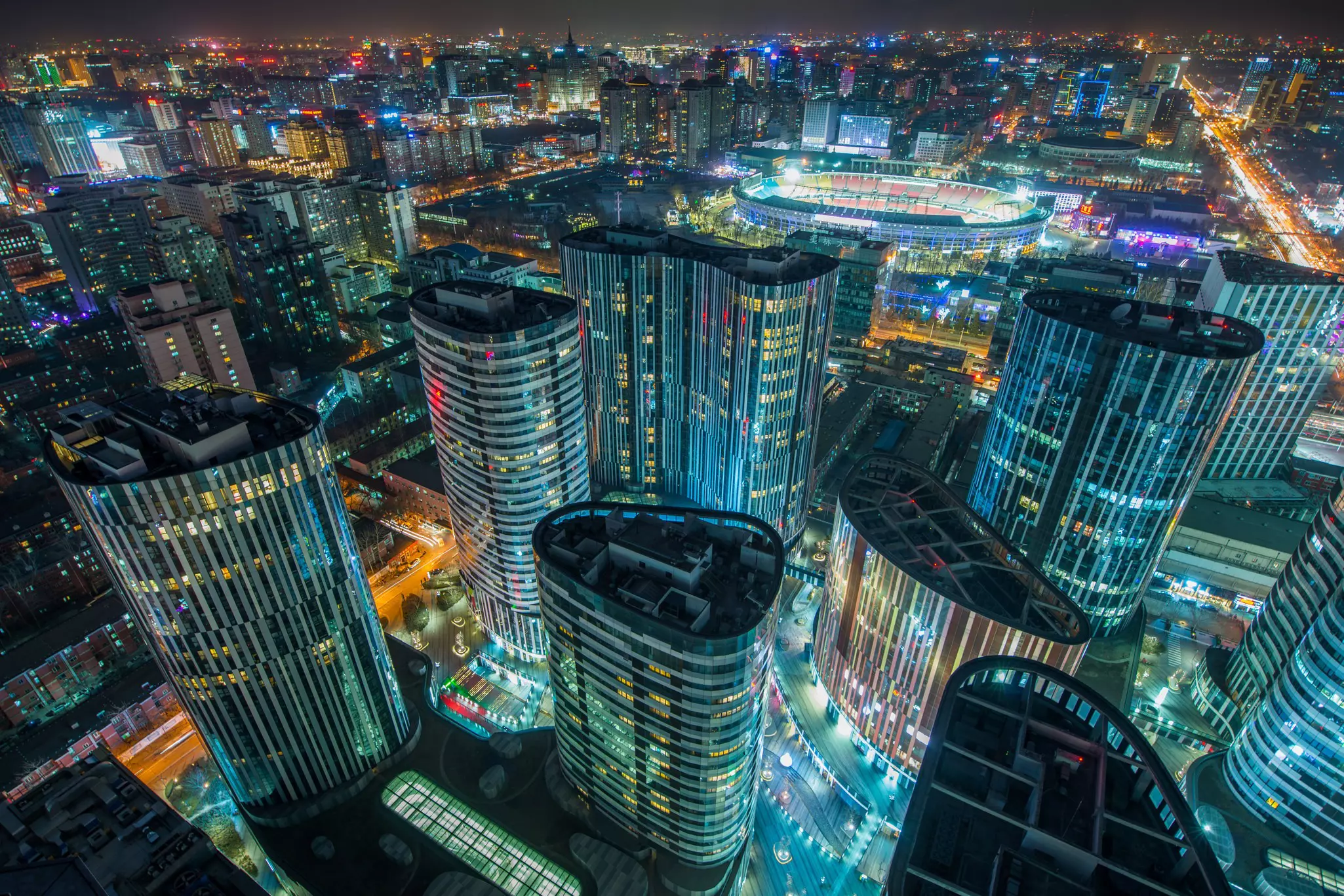 Aerial of the Sanlitun SOHO buildings and the surrounding city lit up at night, Beijing, China.