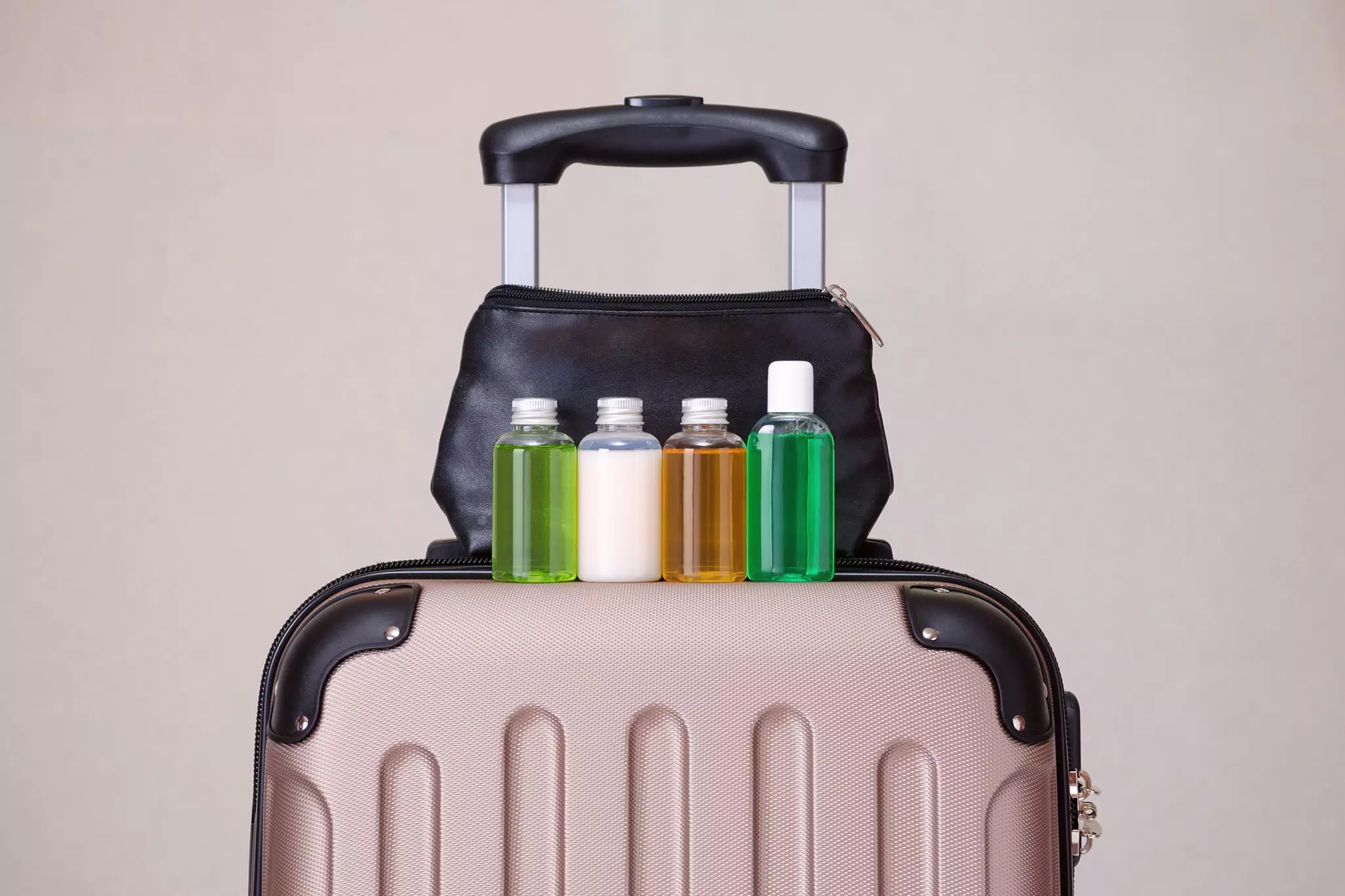 A row of neatly filled bottles of soap and lotions stands on top of a wheelie suitcase