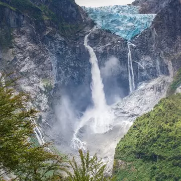 A glacier atop a rockface with a waterfall cascading down
