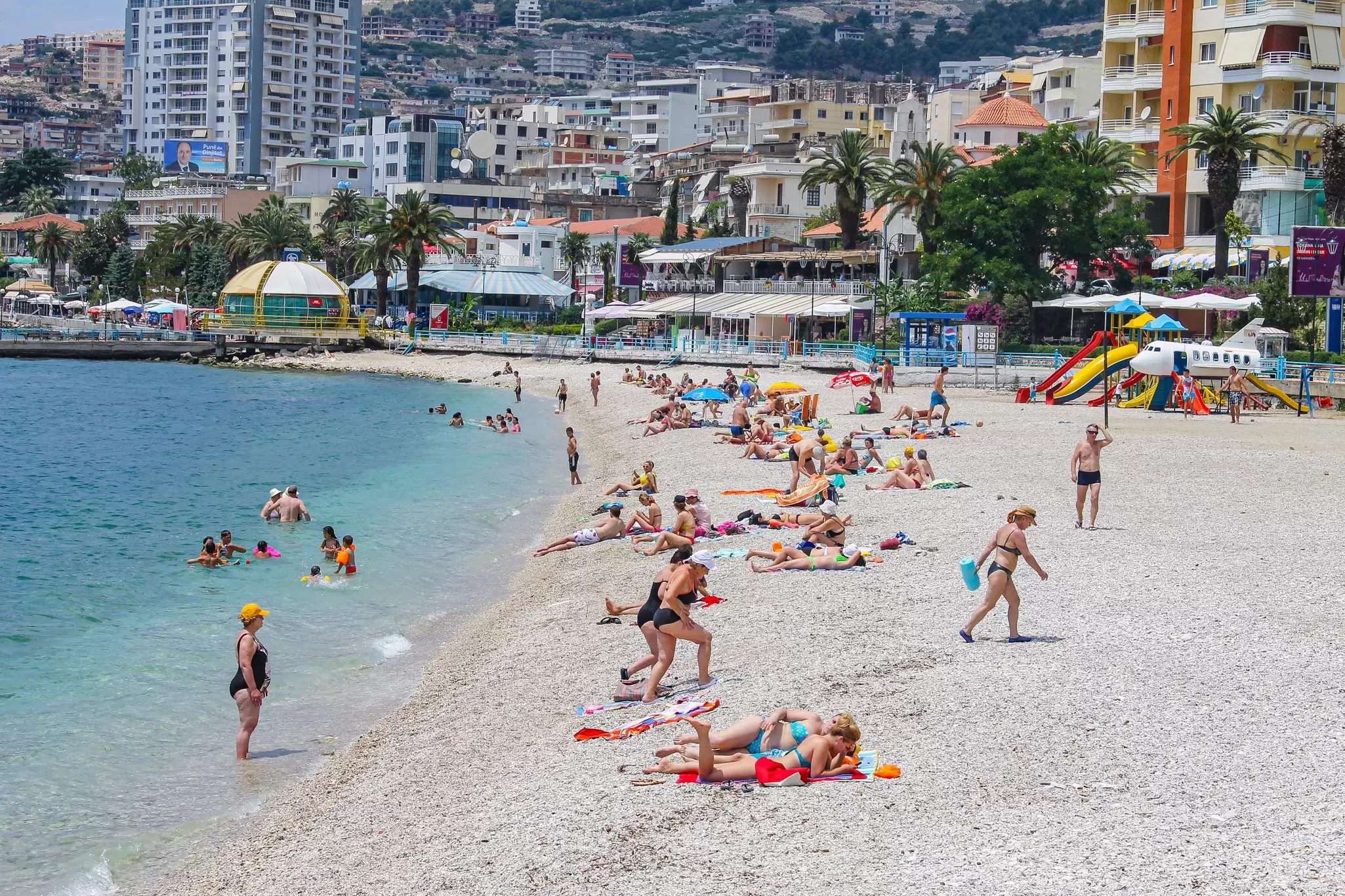 People lounge on the beach and play in the sea on a sunny day in Sarandë, Albania
