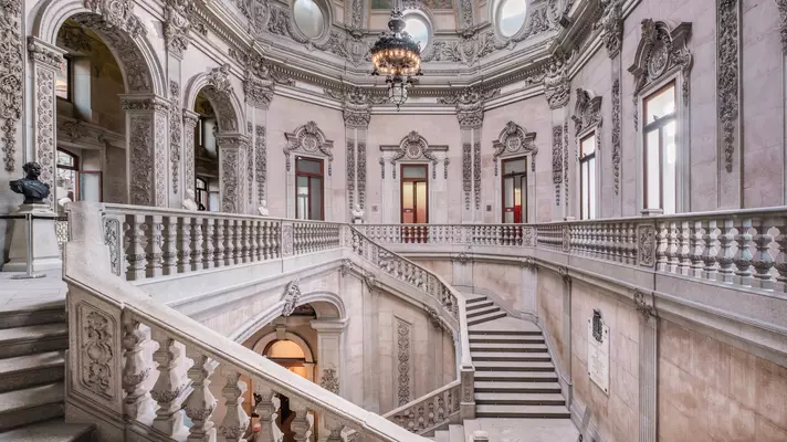 An elaborate blush-toned stone staircase leads to an ornate gallery.