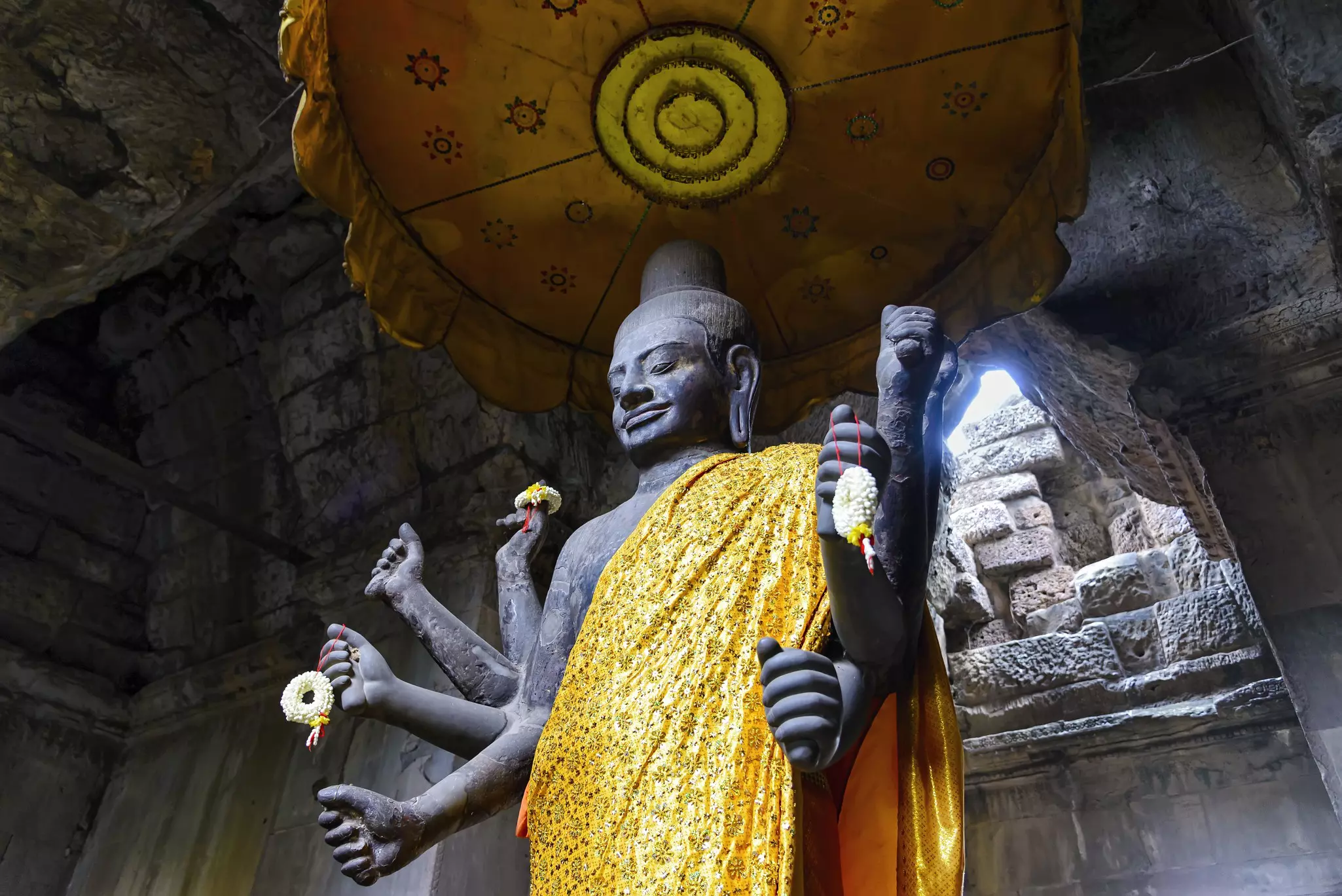 A large statue of a deity with many arms is draped with fabric in a stone temple.