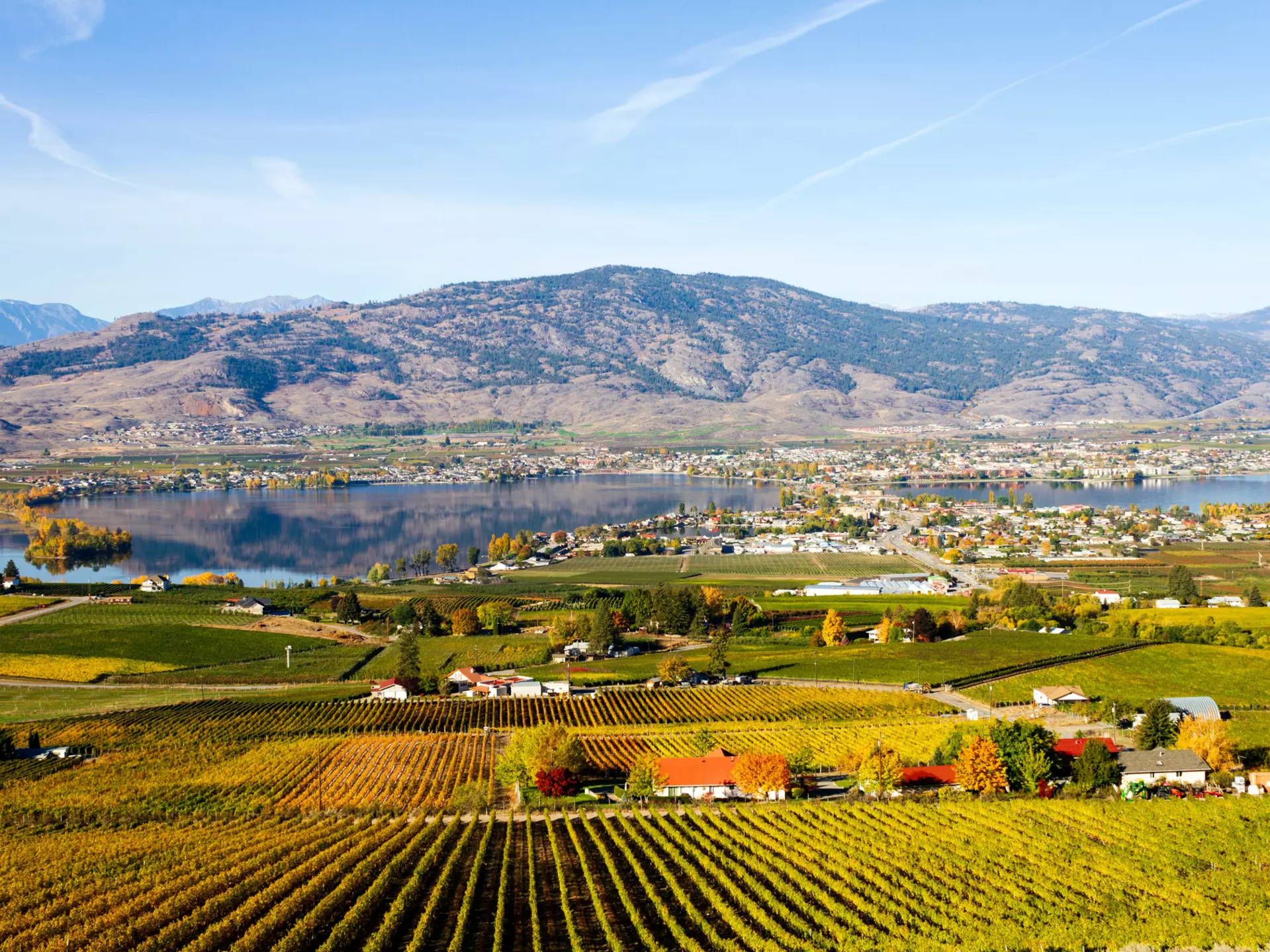 small town surrounding a lake with farms in the foreground and a rising hill in the background.