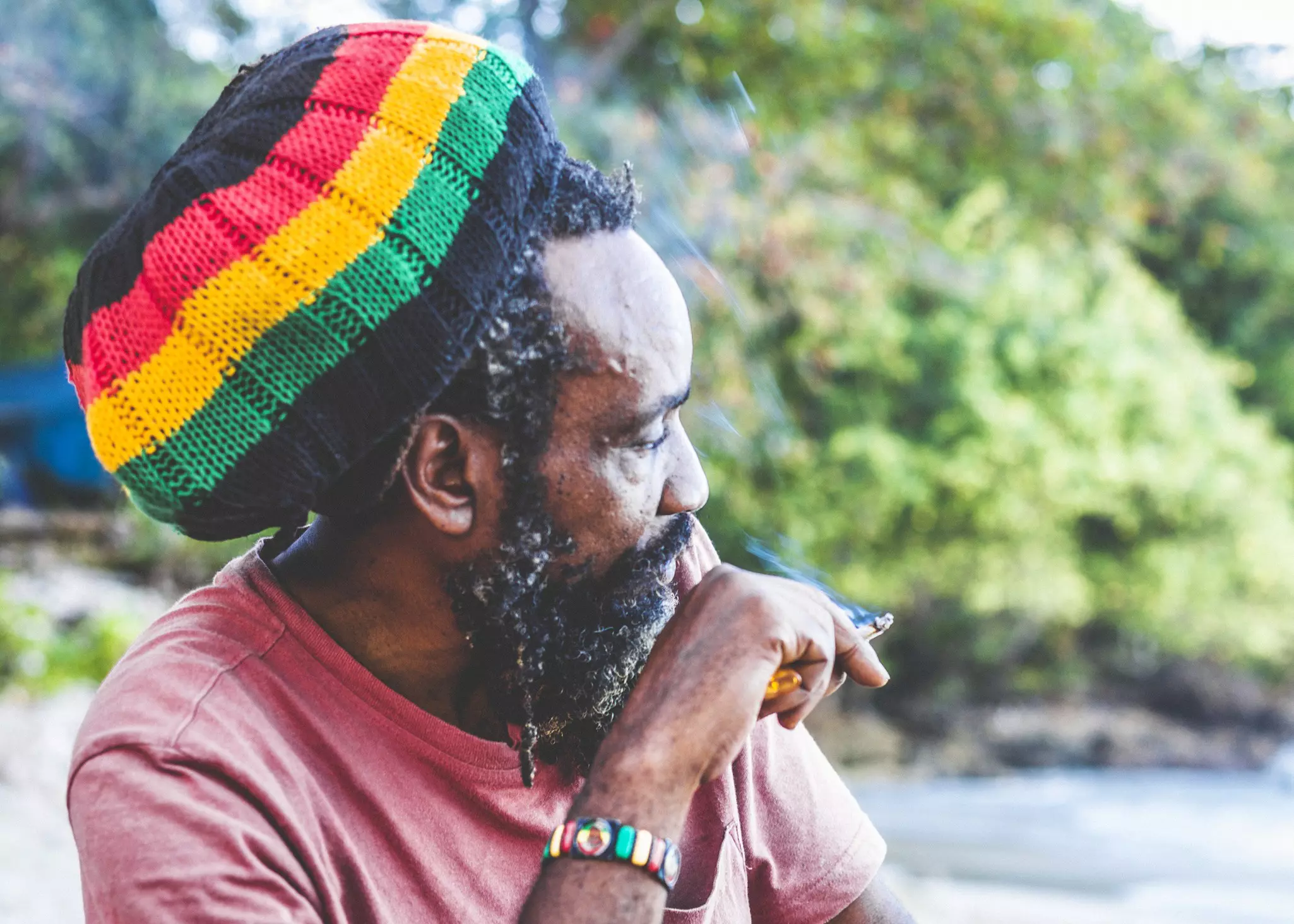 An older Rastafarian man smoking on a beach
