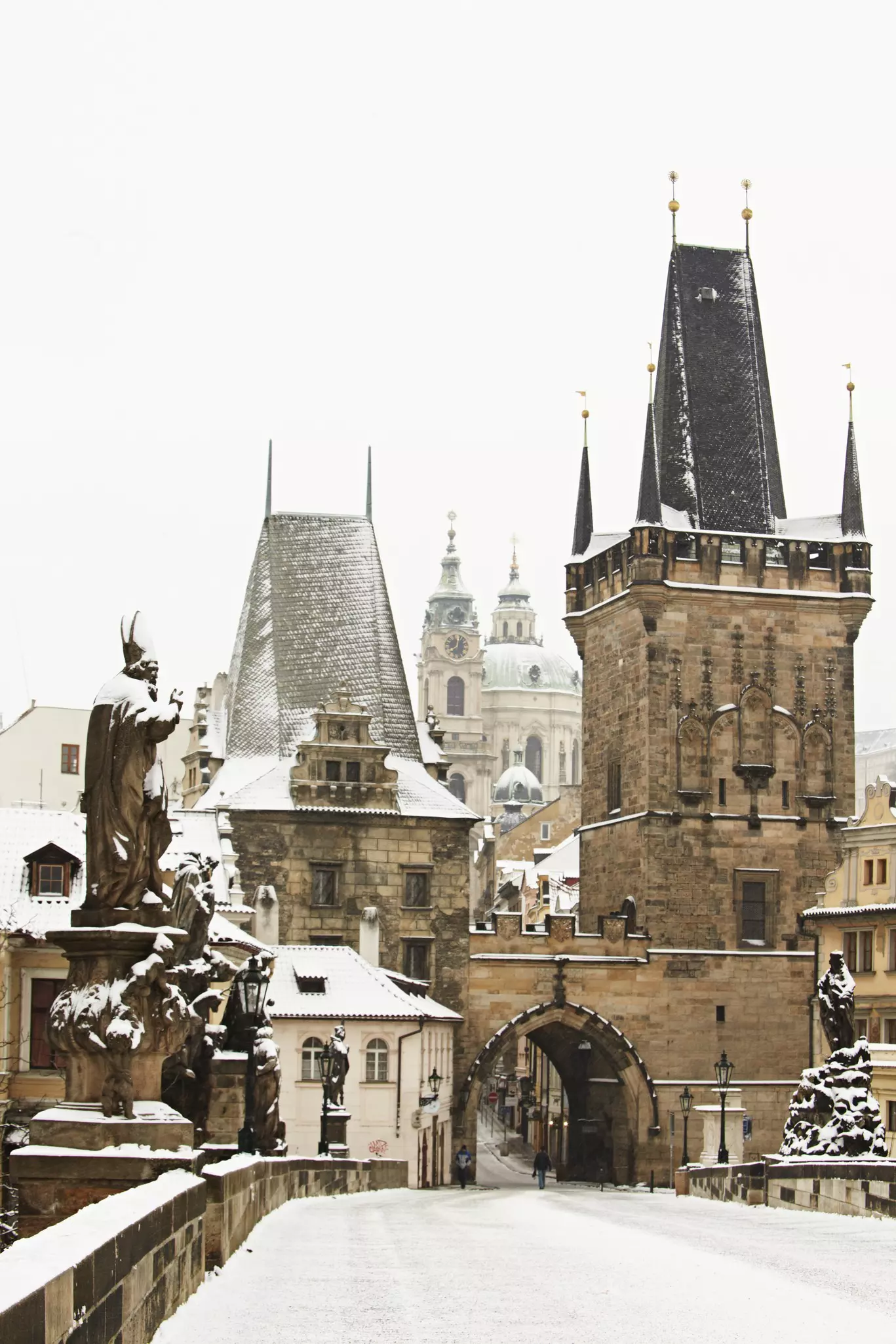 A statue-lined bridge and cathedral covered in snow in winter