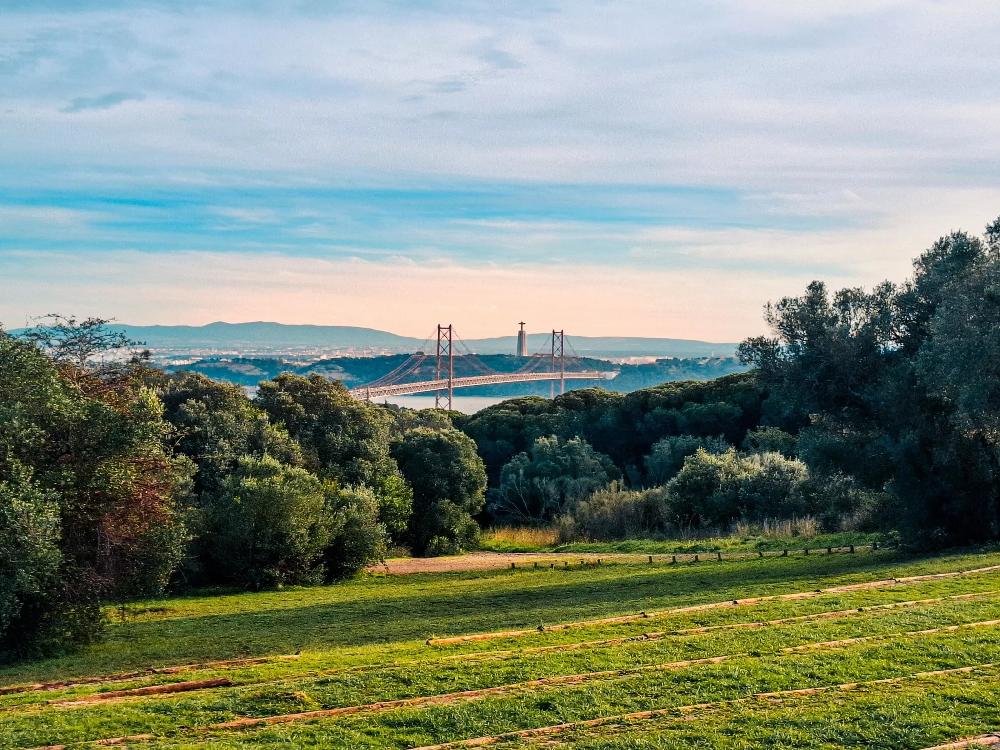 Parkland and woodland above a river with a large suspension bridge over it.