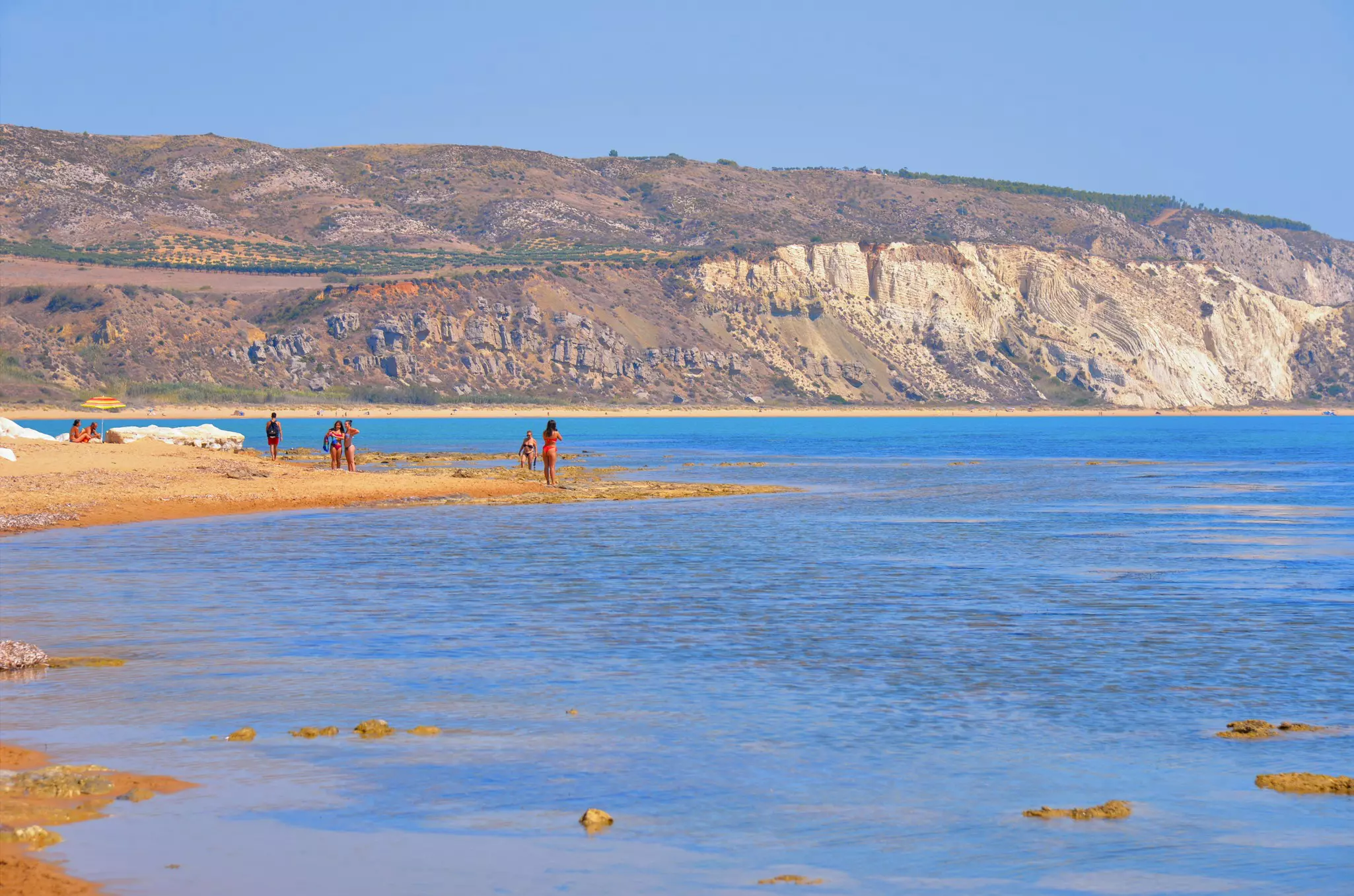 A seascape with people, and clear turquoise water with cliffs in the background.