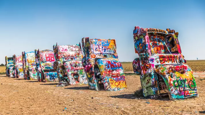 Painted cars are partially buried in a desert as part of an art display.