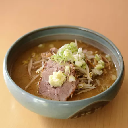 A bowl of miso ramen soup with meat and spring onion. 