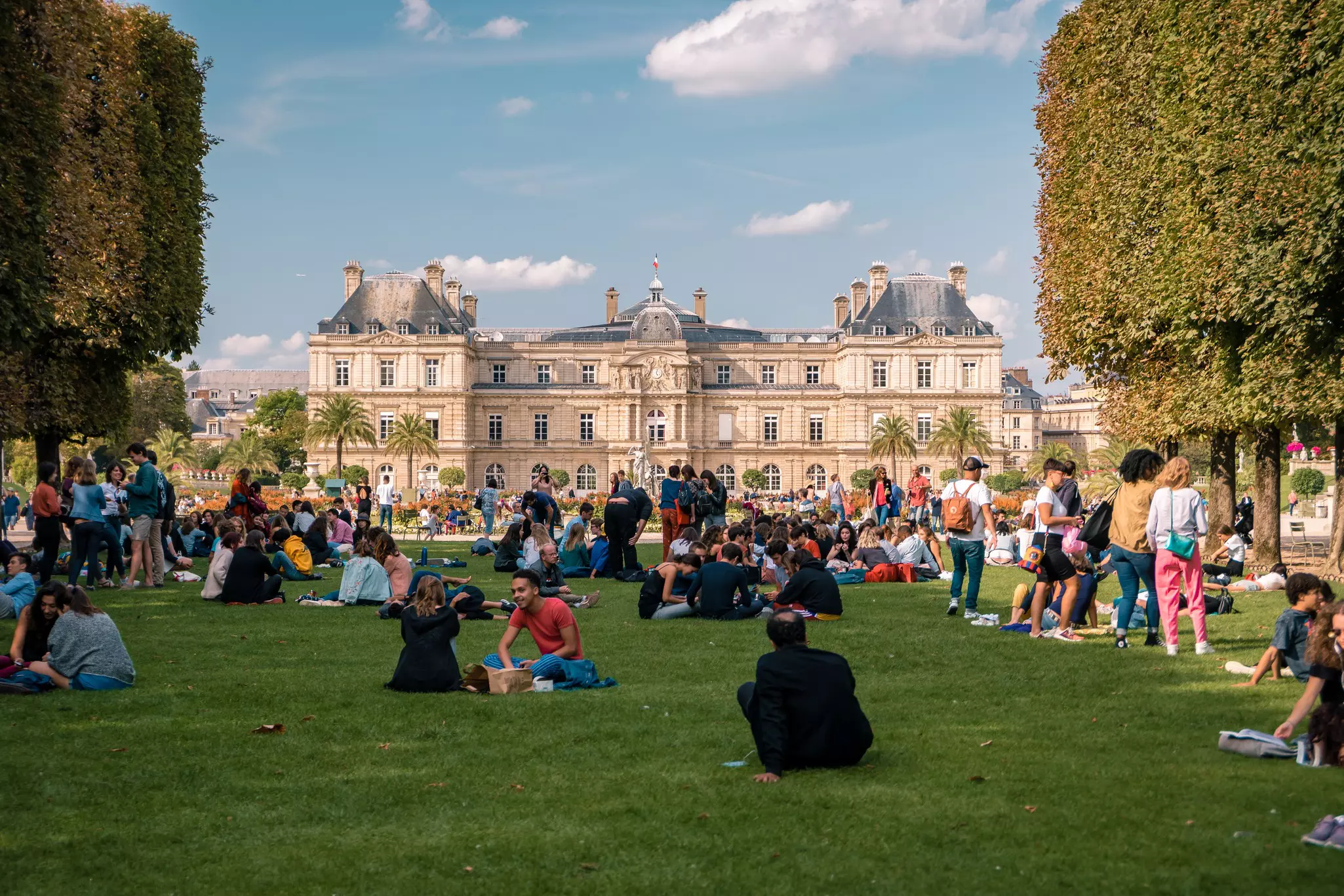 Groups sitting in the Le Jardin Luxembourg during summer, people relaxing in Paris parks.