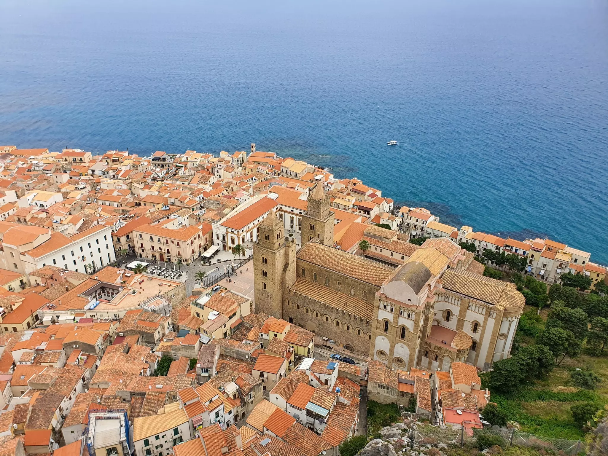 A view looking down on the red roofs of a town, its medieval church rising above the other buildings. The sea is seen beyond the town.