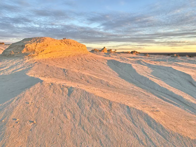 Pink light beams onto sand dunes during a sunset.