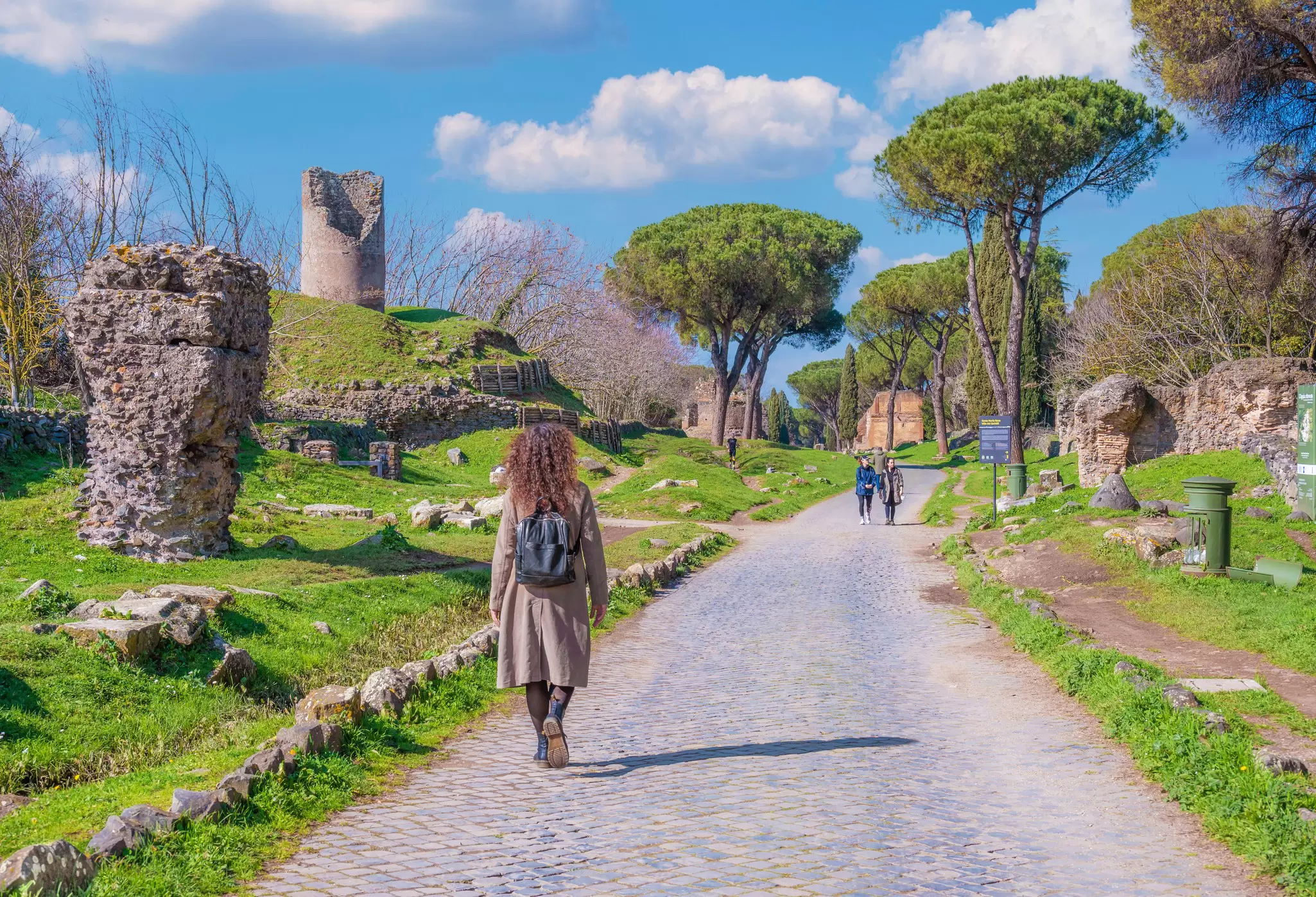People walking by archeological ruins on the Via Appia Antica in Rome, Italy.