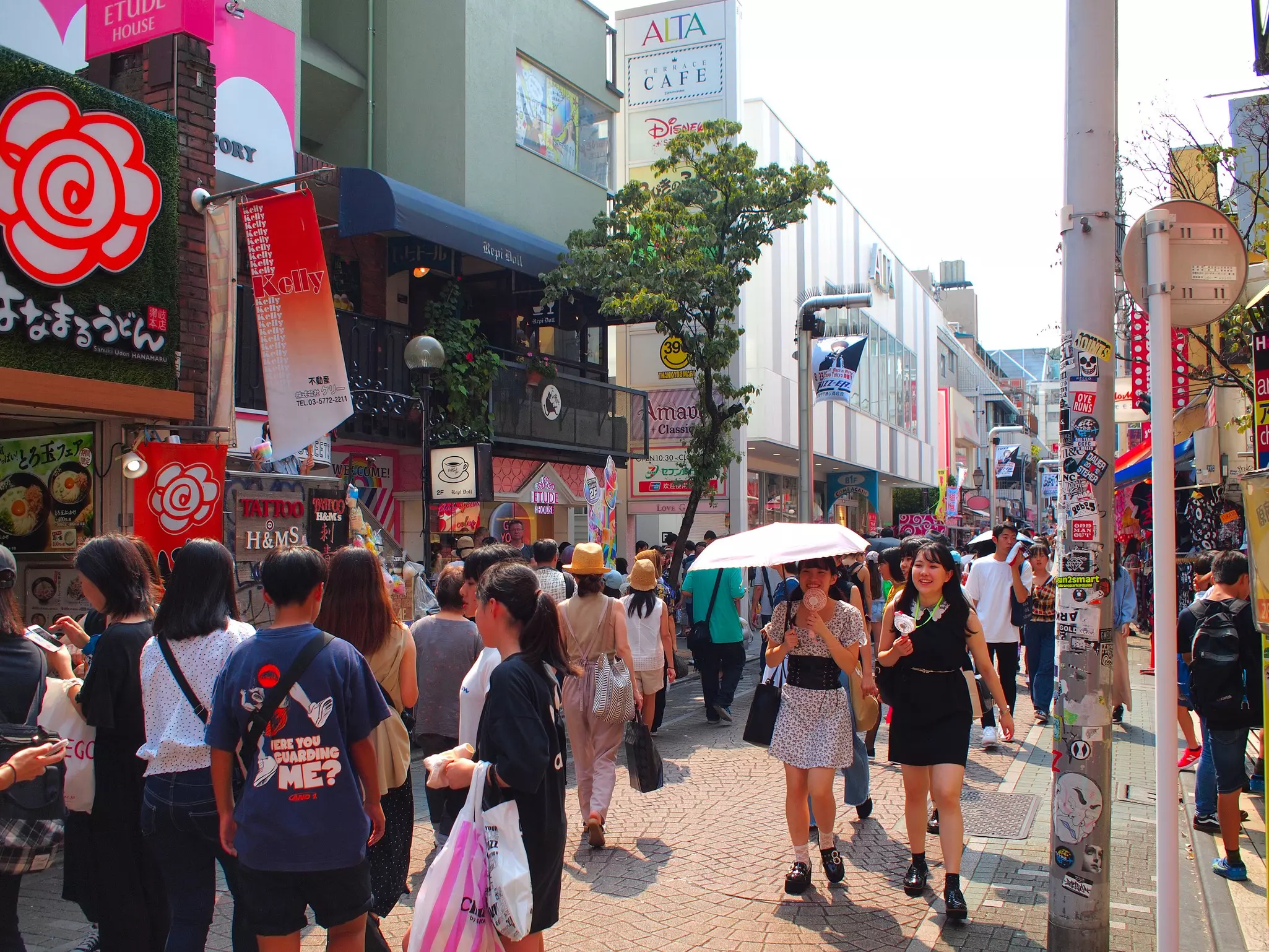 People walk past stores and restaurants on a crowded pedestrianized street in a city.