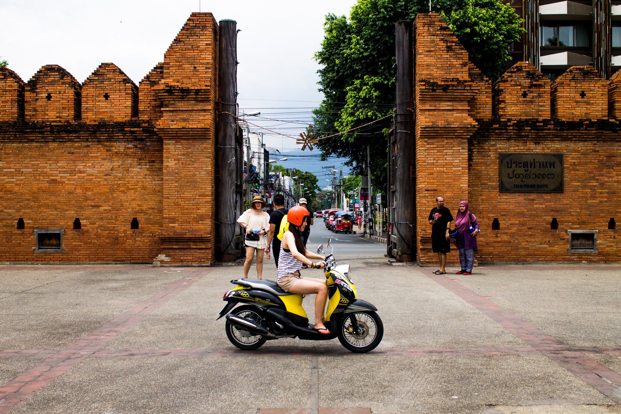 Group of tourists looking around the Thapae gate and one girl riding by on a moped. Chiang Mai, Thailand.