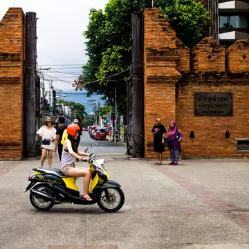 Group of tourists looking around the Thapae gate and one girl riding by on a moped. Chiang Mai, Thailand.