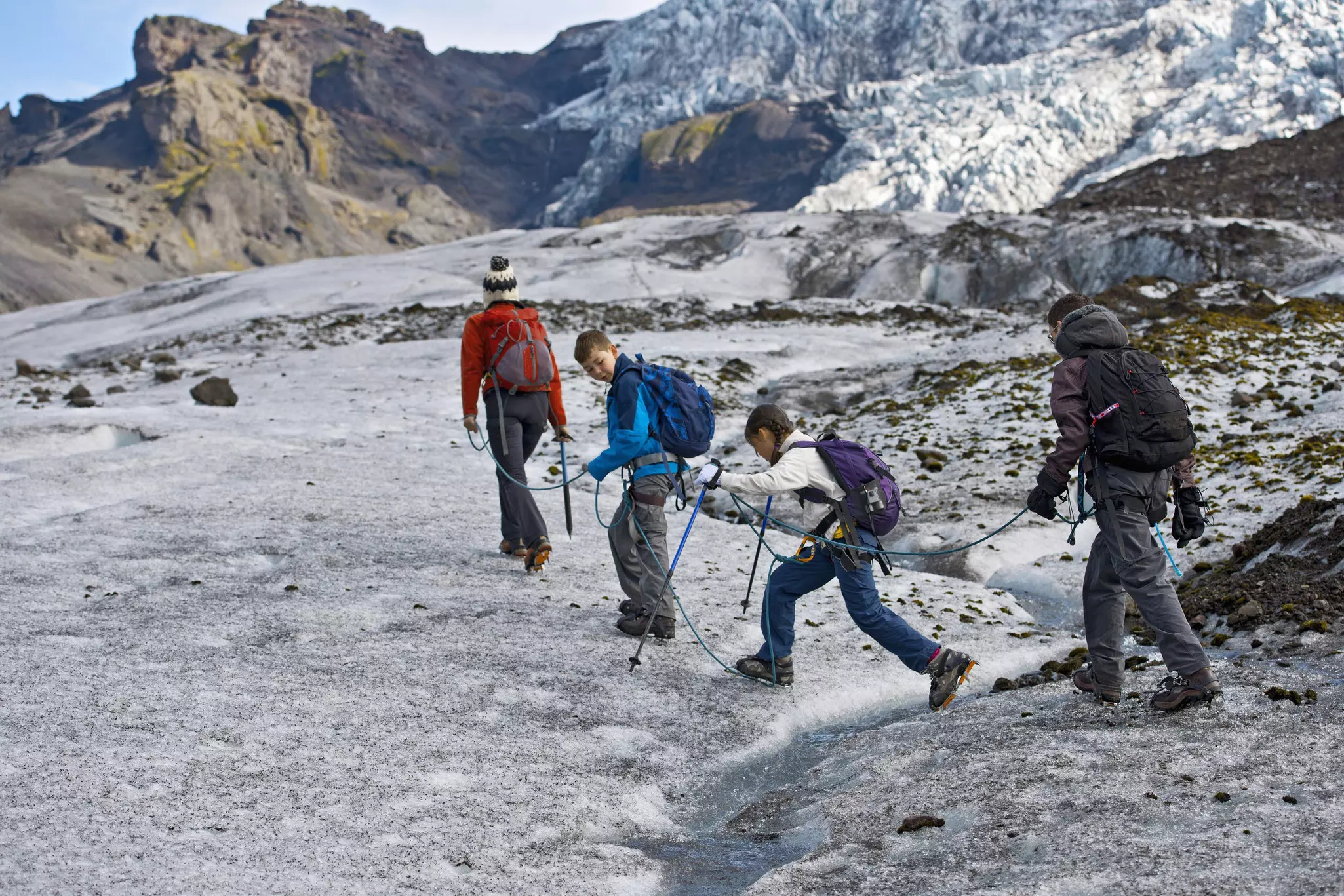 A family walking tethered together on a glacier.