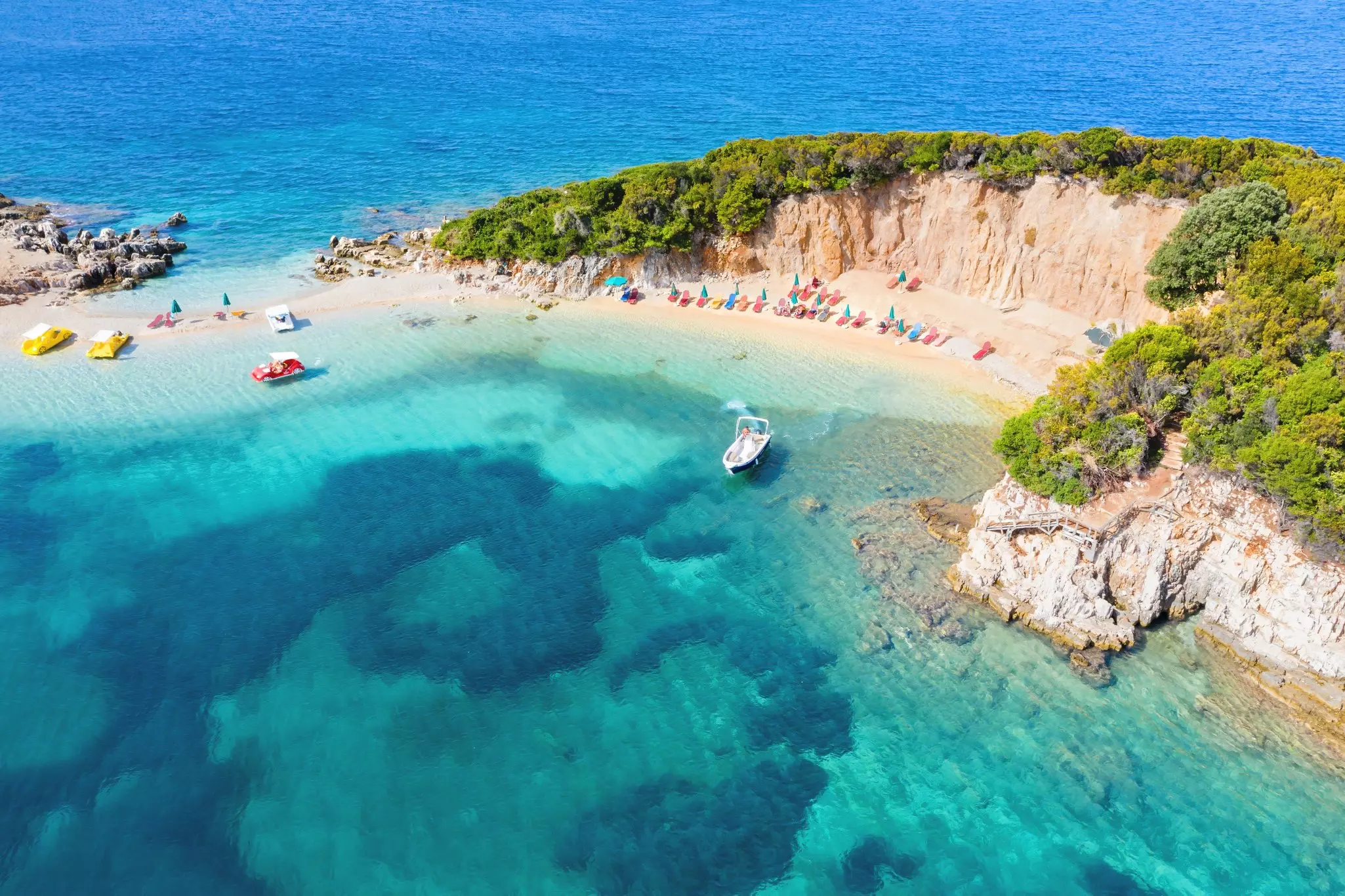 An overhead shot of a narrow beach on a spit of land, with boats moored in the water beside the sand.