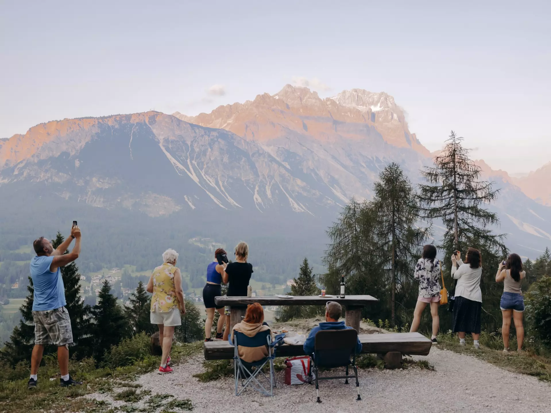 People sit in camp chairs and stand at an overlook for a mountain viewpoint.