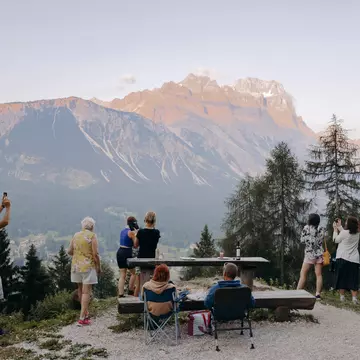 People sit in camp chairs and stand at an overlook for a mountain viewpoint.