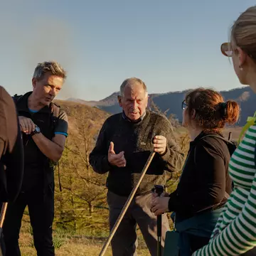 A group of hikers pause on the trail to listen to a guide tell a story about their route.