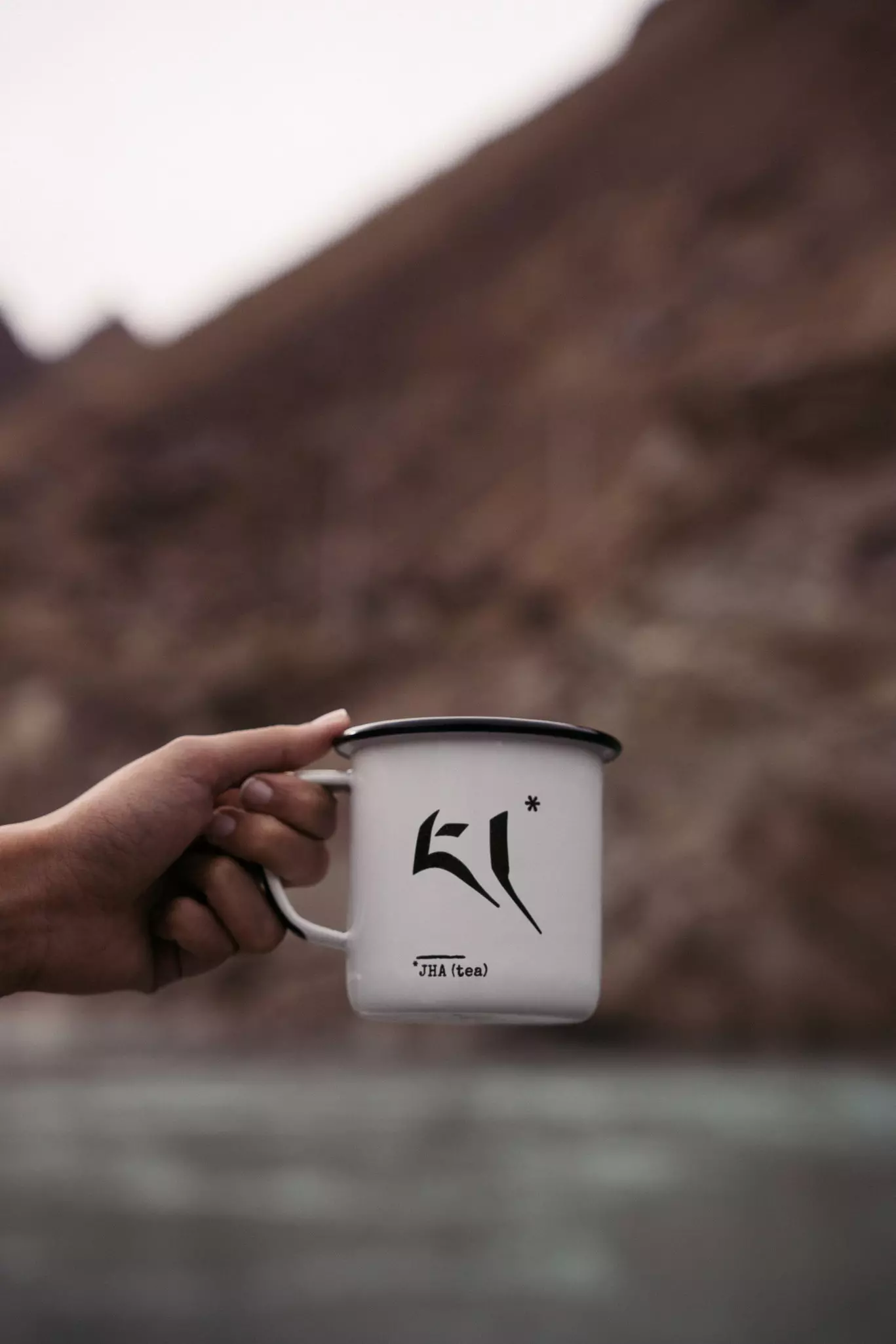 A hand holding a mug that says "JHA (tea)" on it.