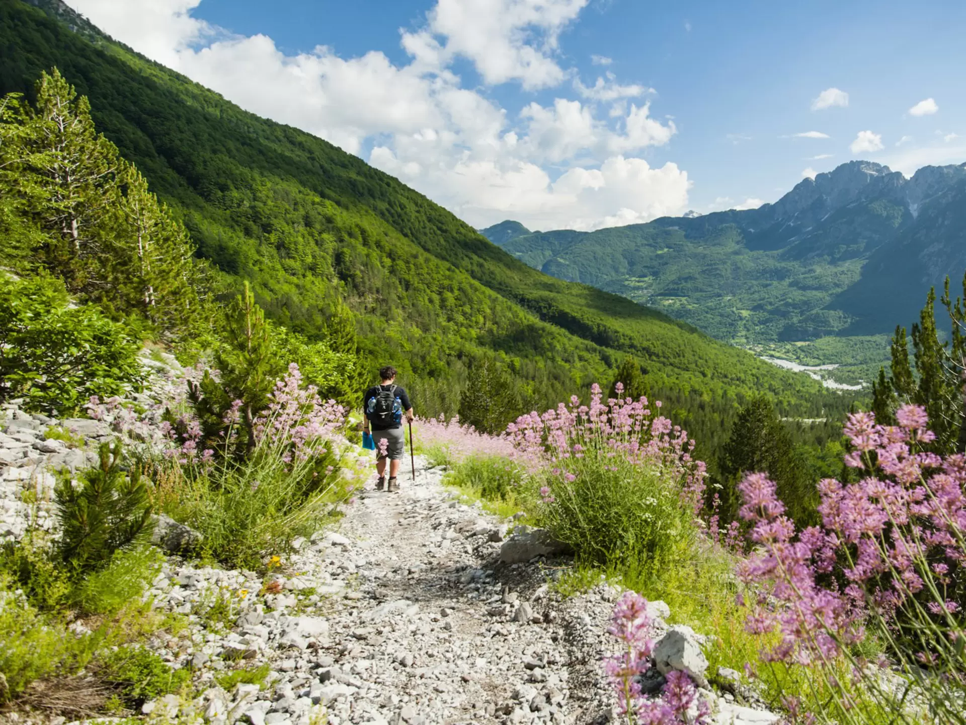 A hiker walking along a gravel trail through mountains; the Qafae Pëjes pass  near the village of Theth, Albania