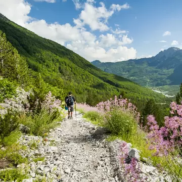 A hiker walking along a gravel trail through mountains; the Qafae Pëjes pass  near the village of Theth, Albania