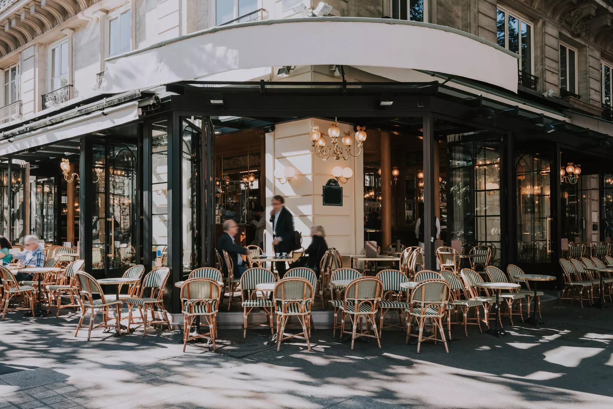 Typical view of a Parisian brasserie with outdoor tab;es and striped chairs facing the street.