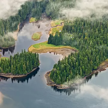 Aerial view of mist hovering around lakes, forest and mountains in a national park in Alaska.