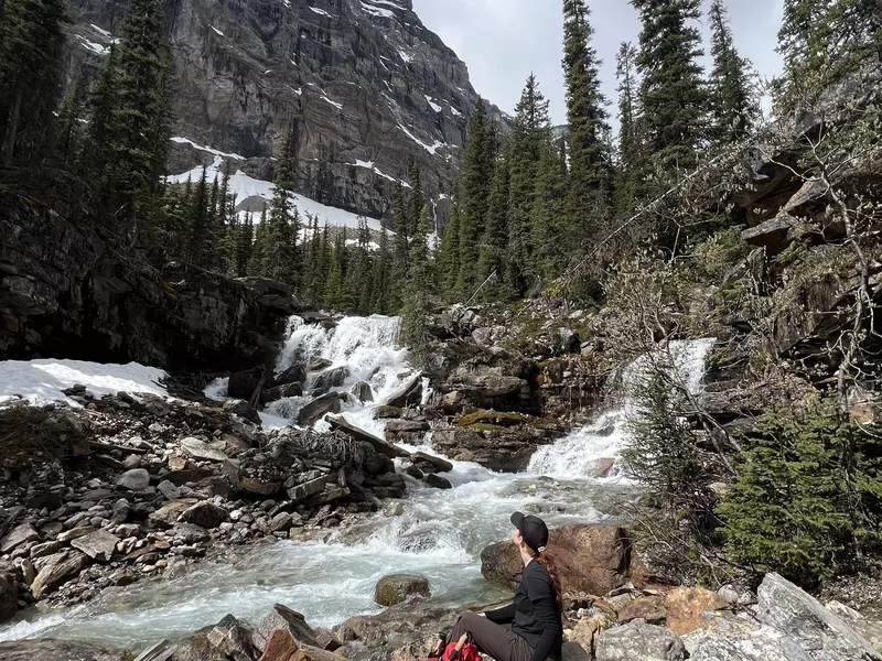 A hiker rests beside a rushing mountain stream