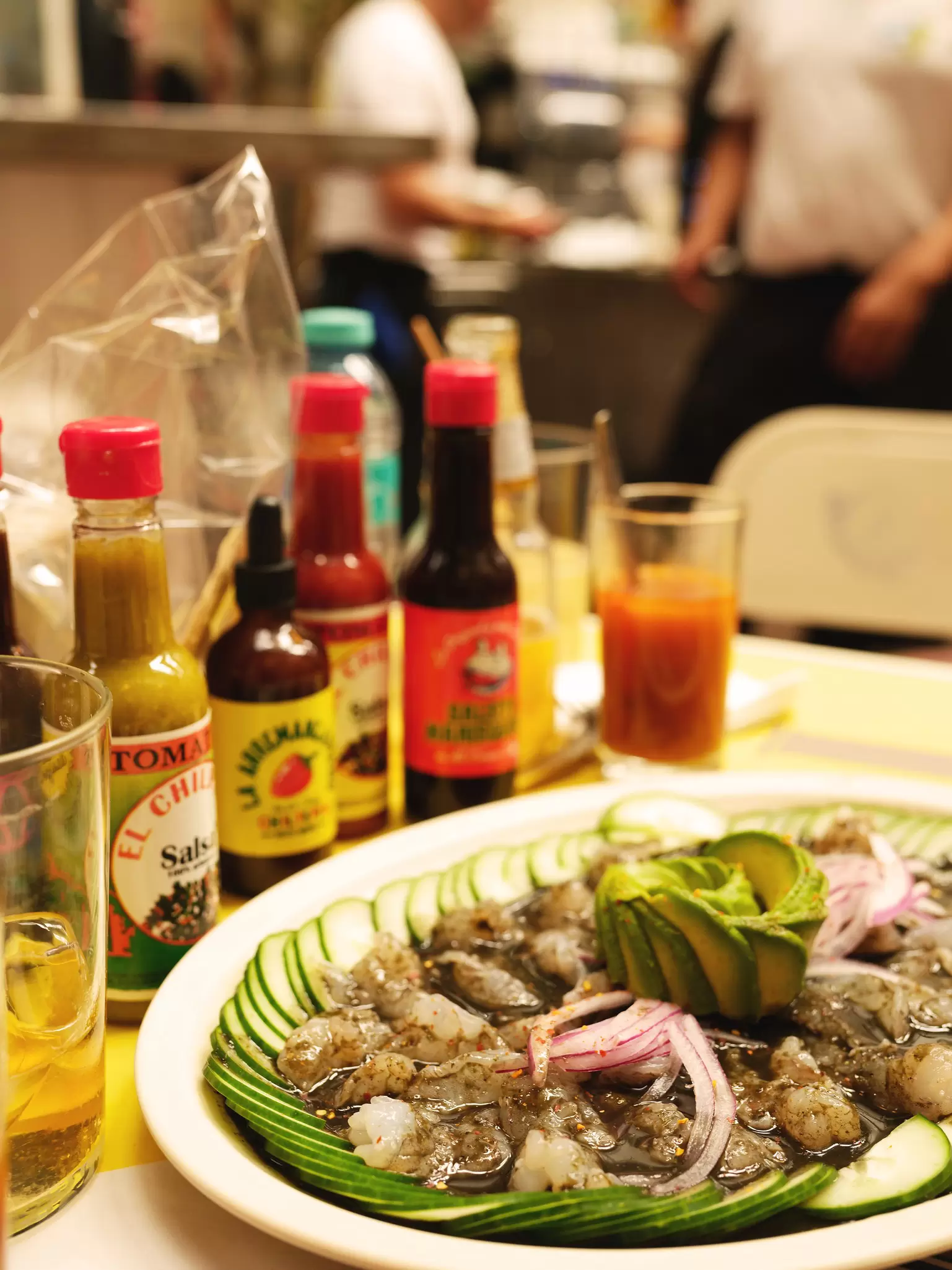 Close up of fresh seafood dish with bottles of sauces behind and out of focus kitchen staff at Mi Compa Chava in Roma Norte, CDMX