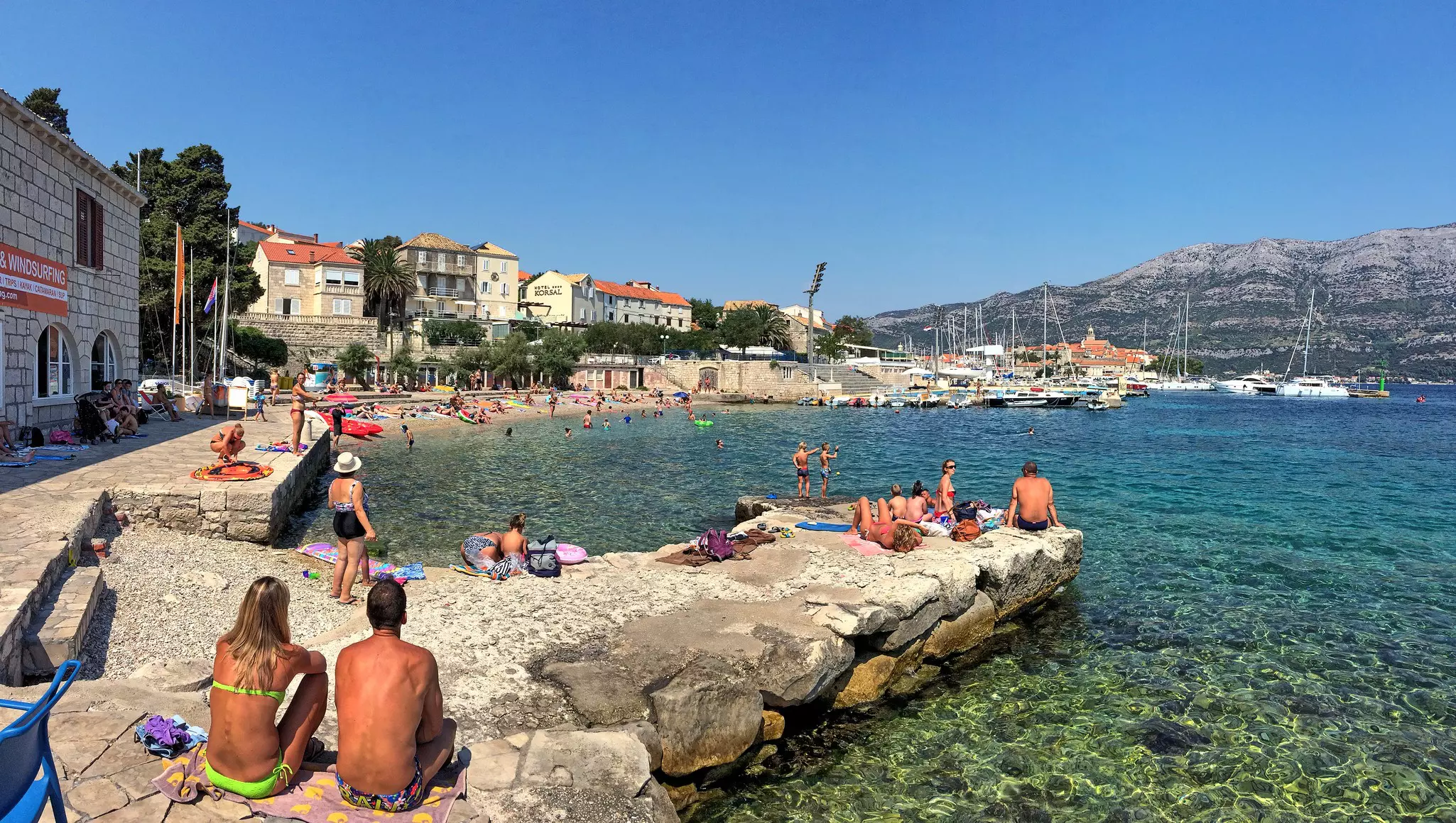 People sunbathe in their swimwear on the rocky coastline near Korčula Town, Croatia.