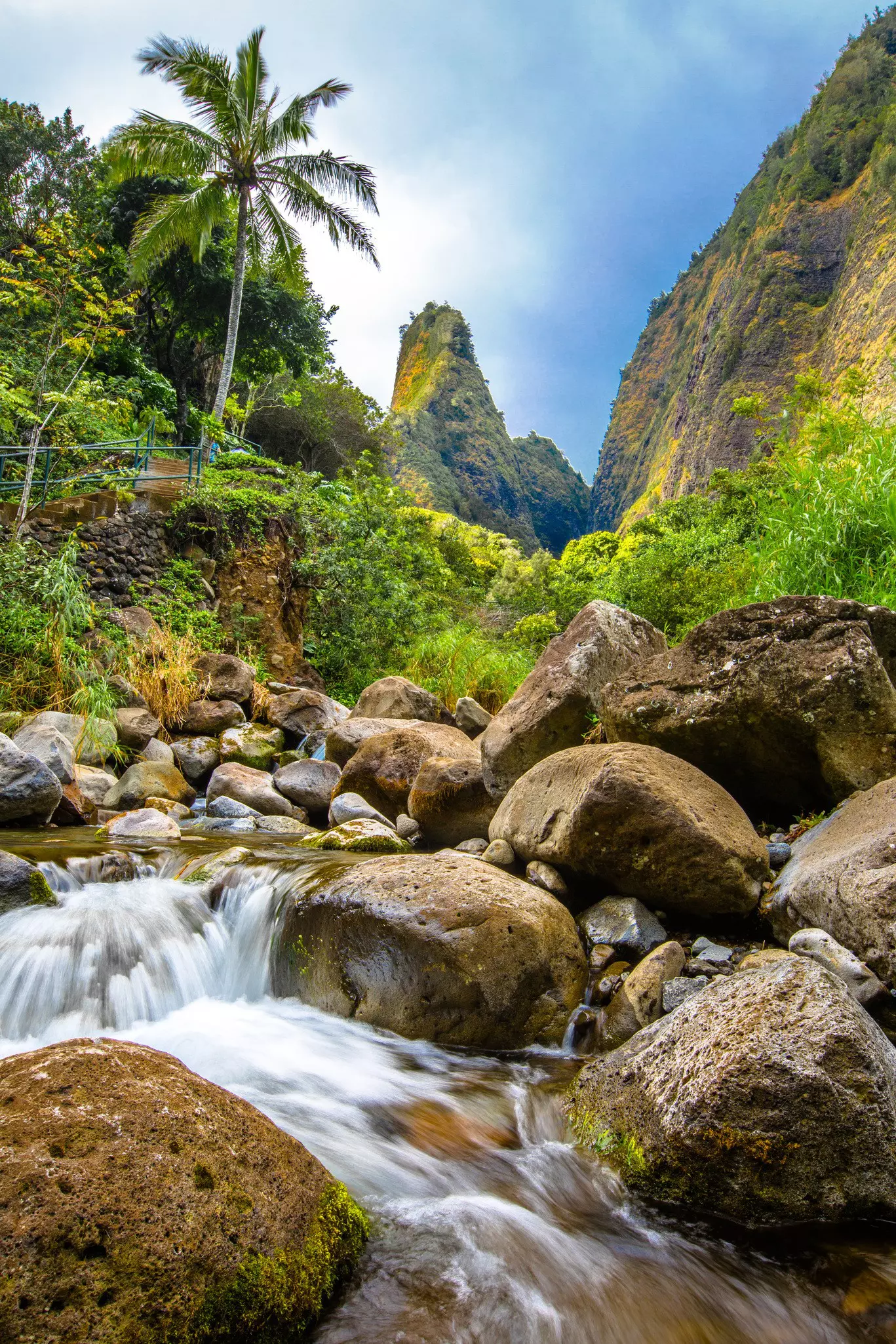 A pointed pinnacle of rock covered in greenery stands tall among lush rainforest with a river running through it.