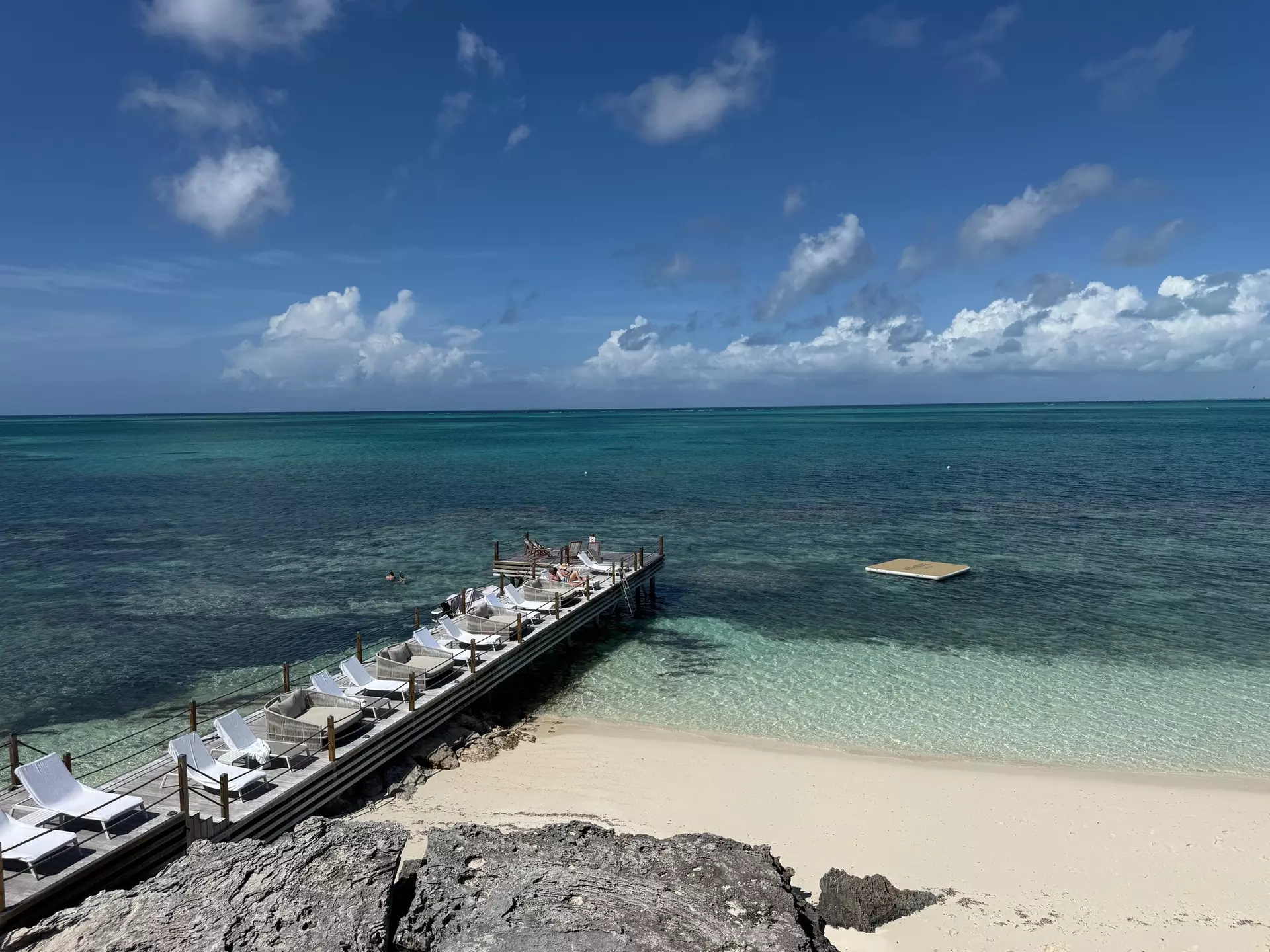 A narrow wooden pier lined with sunloungers stretching out into the ocean