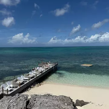 A narrow wooden pier lined with sunloungers stretching out into the ocean