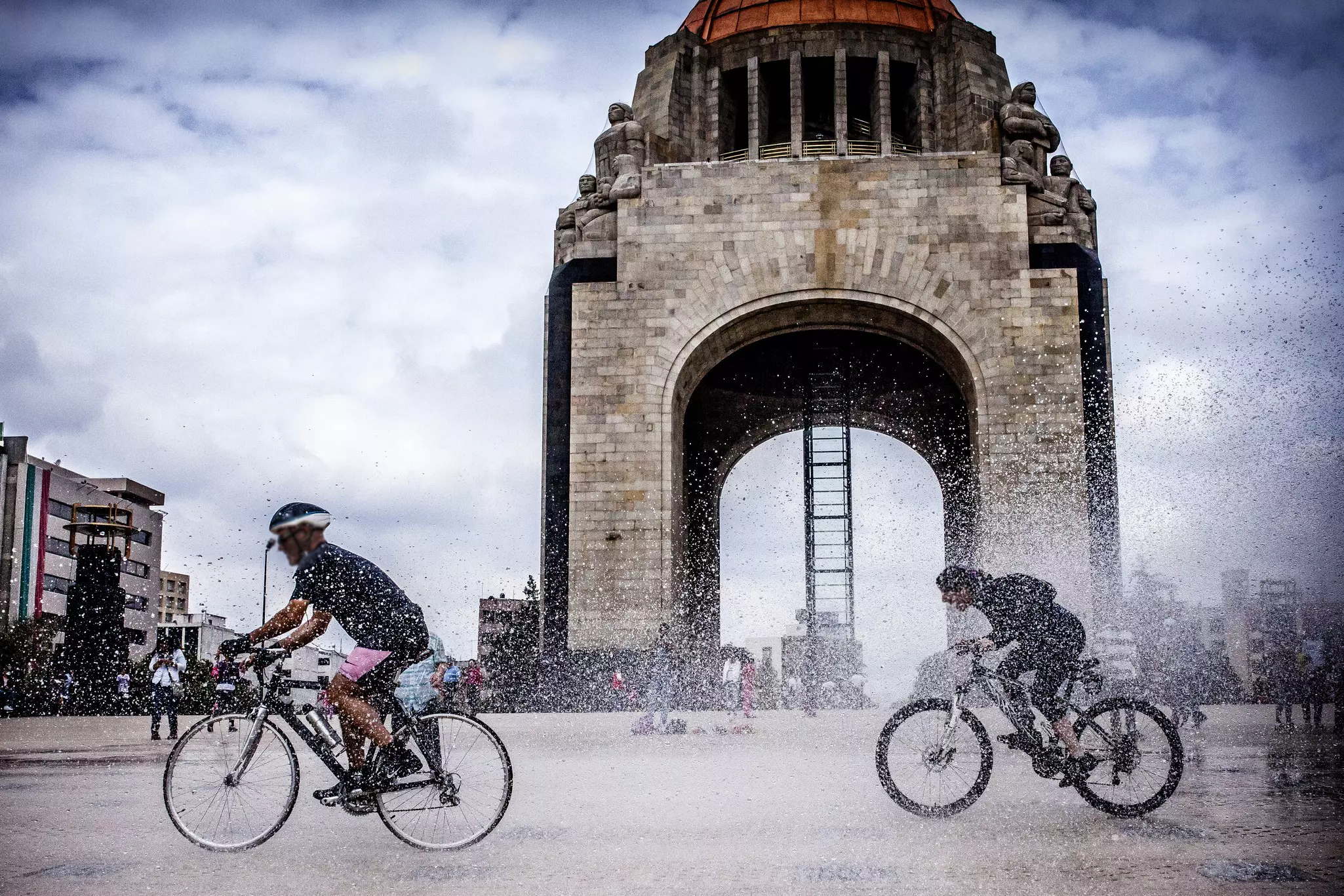 Cyclists splash water as they ride past the Monumento a la Revolución in Mexico City