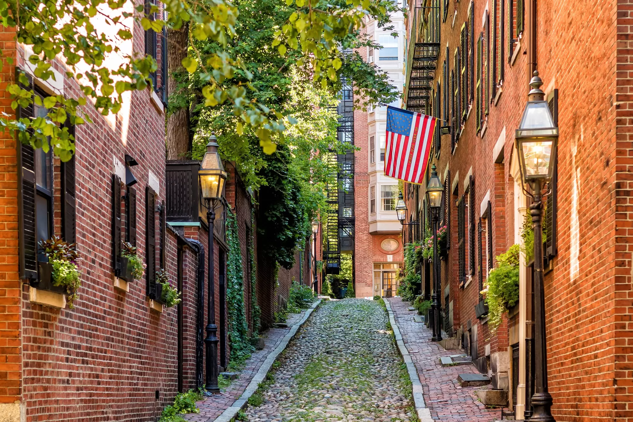 A narrow, cobbled street with red-brick buildings either side and an American flag hanging off one of them.