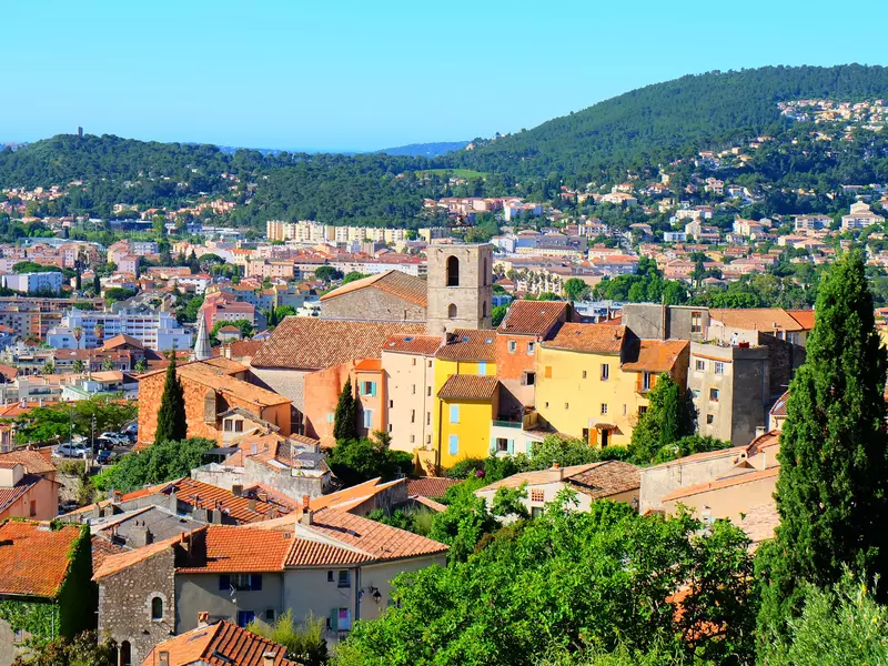 A view from a hill of a rustic French town surrounded by trees. 