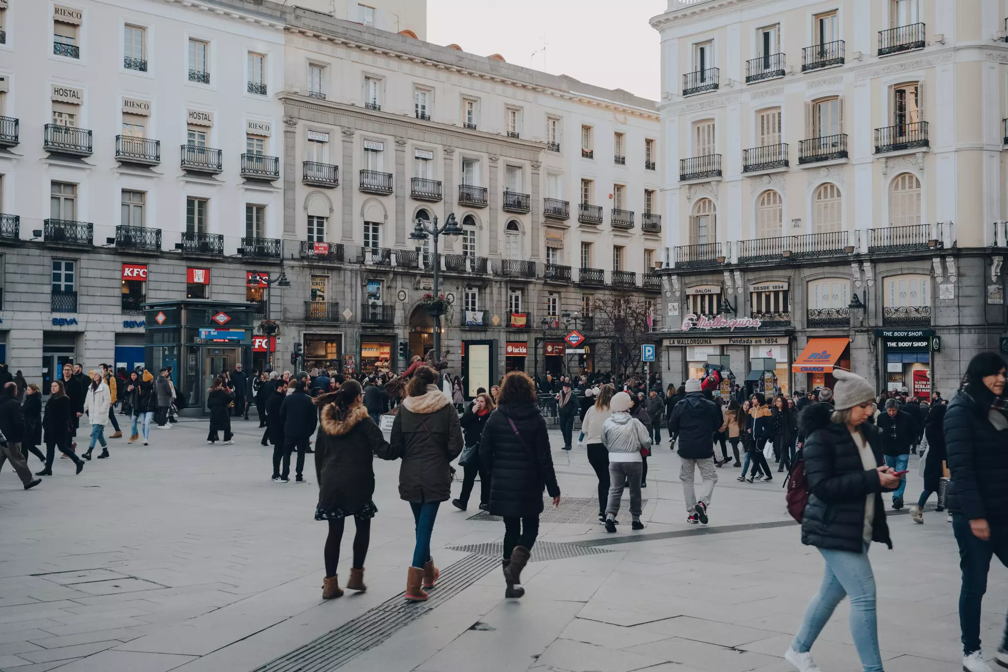 People in winter coats walk in a city square