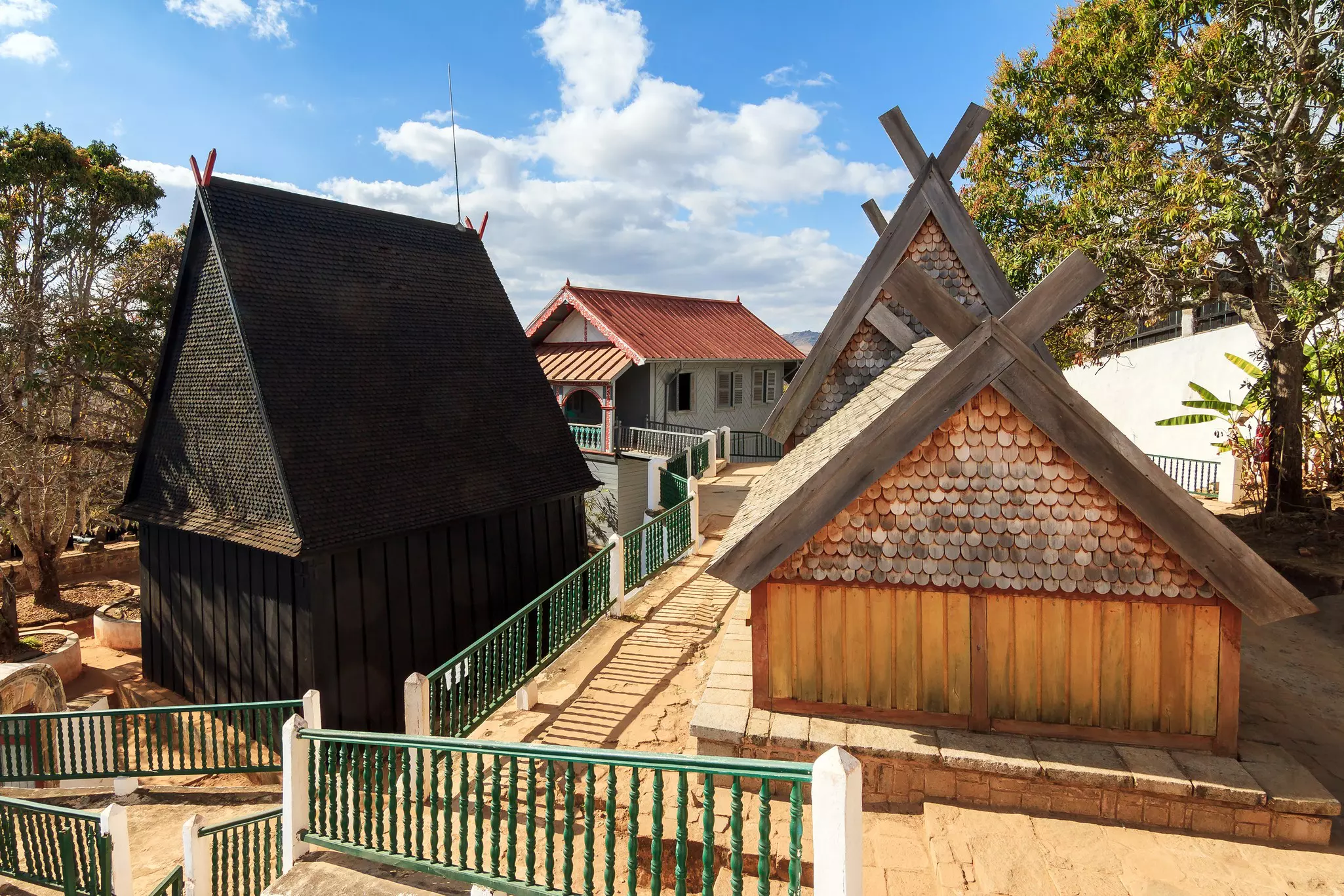 Two historic buildings with peaked roofs and wooden shingles, part of the historic site of Ambohimanga in Madagascar.