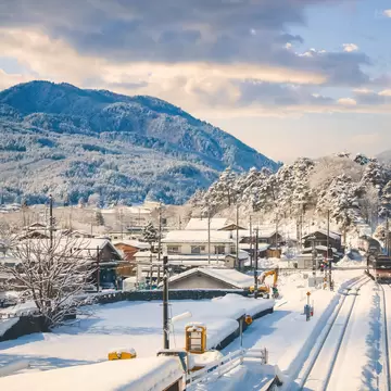Train on snowy tracks beside snow-covered rooftops and forested mountains in Takayama, Japan, in winter