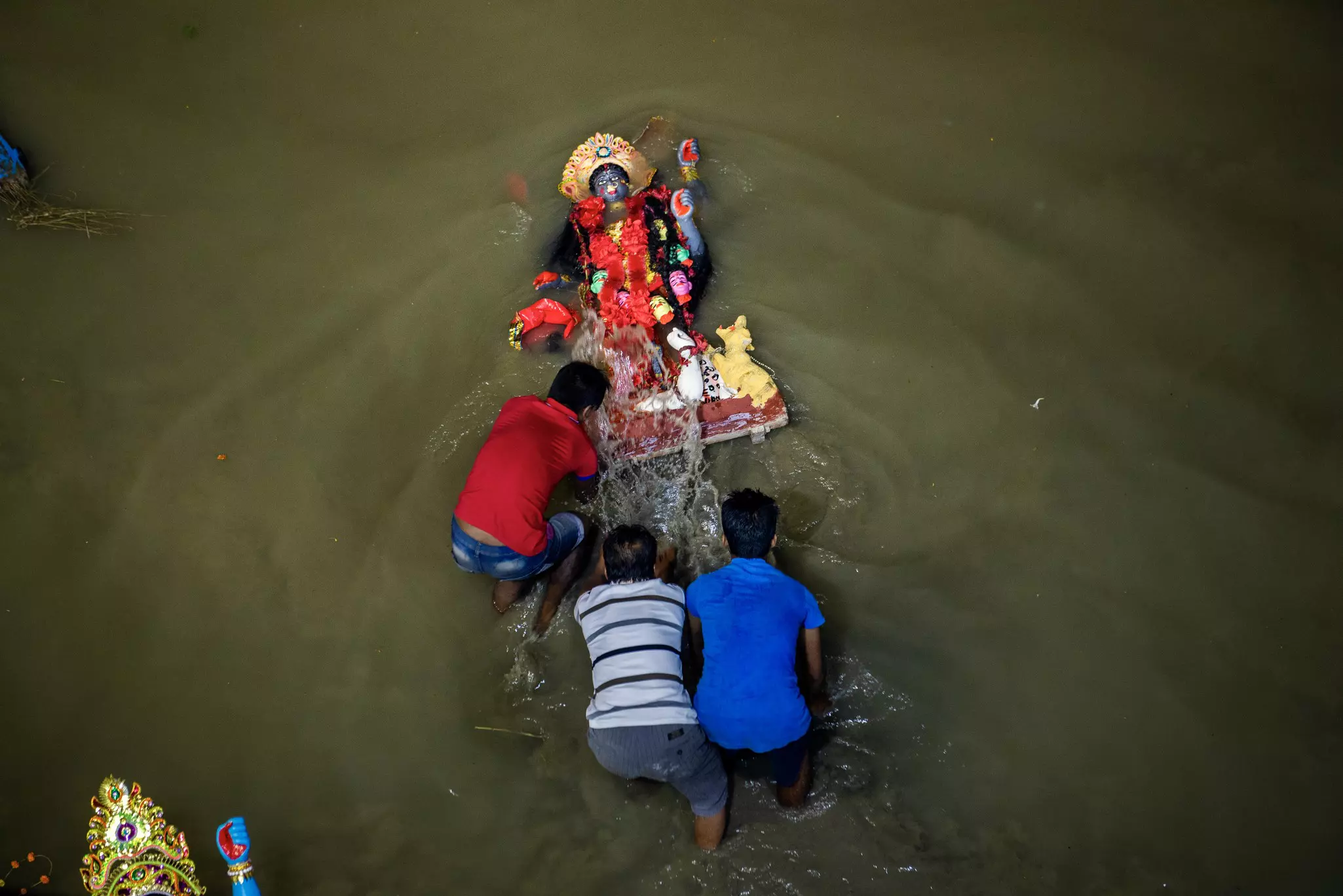 Men immerse a statue of a Goddess into a river