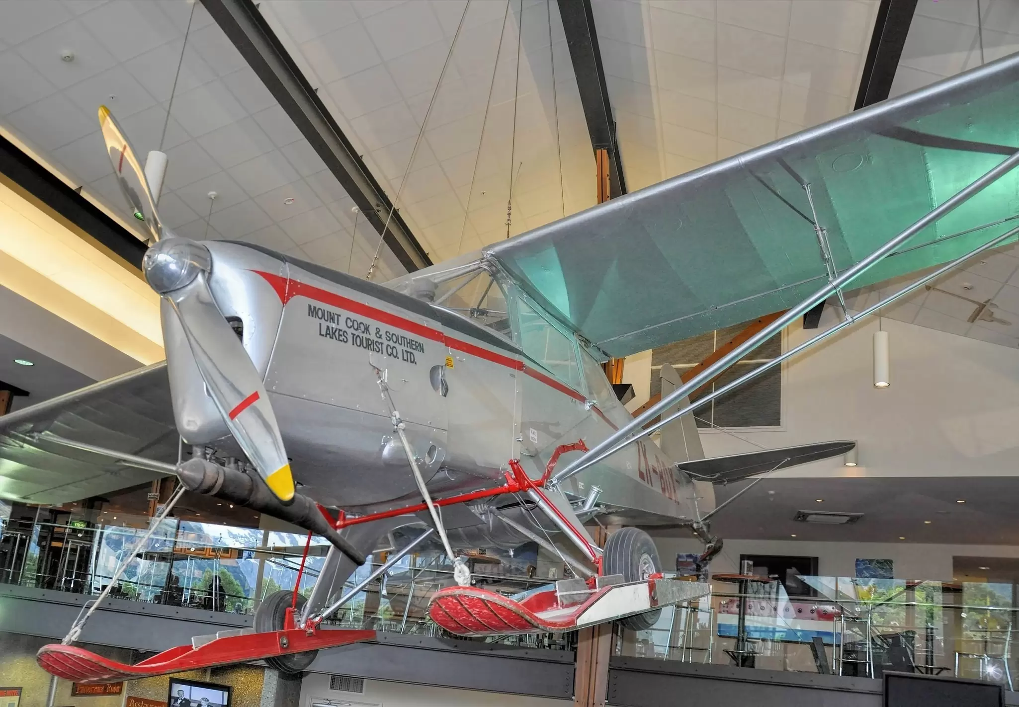 A large silver-and-red aircraft suspended from the ceiling in a museum.