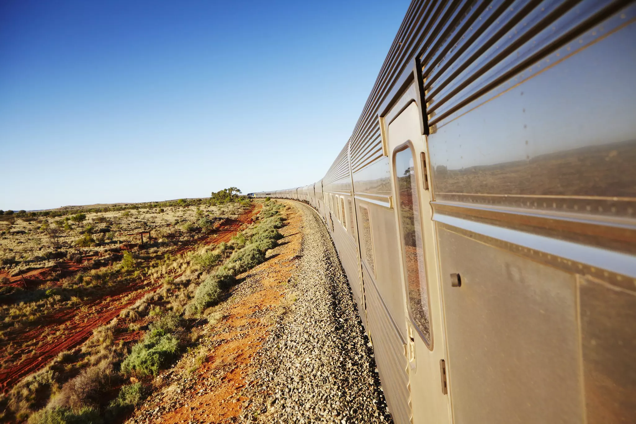 A train runs through a vast landscape of scrub and red earth.